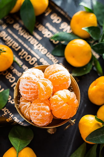 Fresh peeled clementines in a gold bowl with whole tangerines and green leaves