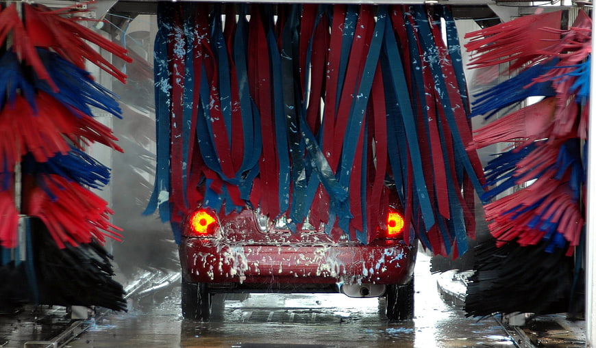 Red car being washed by spinning brushes in automatic car wash