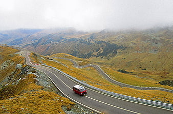 Red Van Driving on Winding Mountain Road in Foggy Landscape