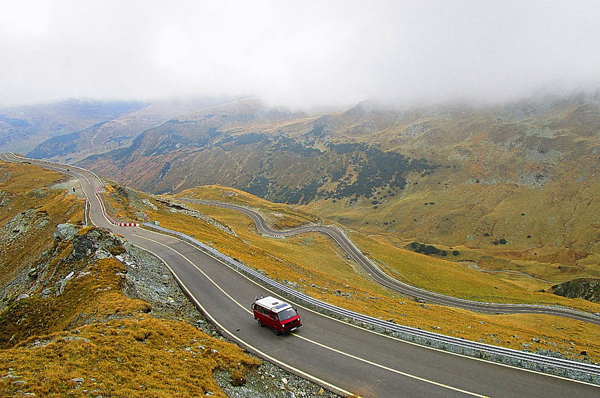 Red Van Driving on Winding Mountain Road in Foggy Landscape