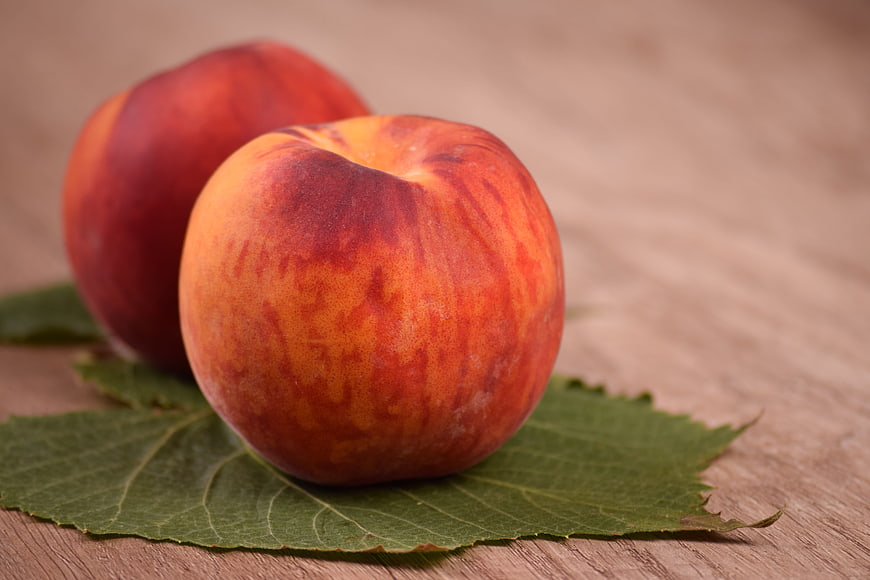 Fresh ripe peaches on wooden table with green leaf