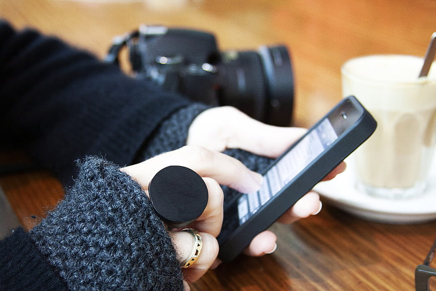 Woman using smartphone with coffee and camera on table
