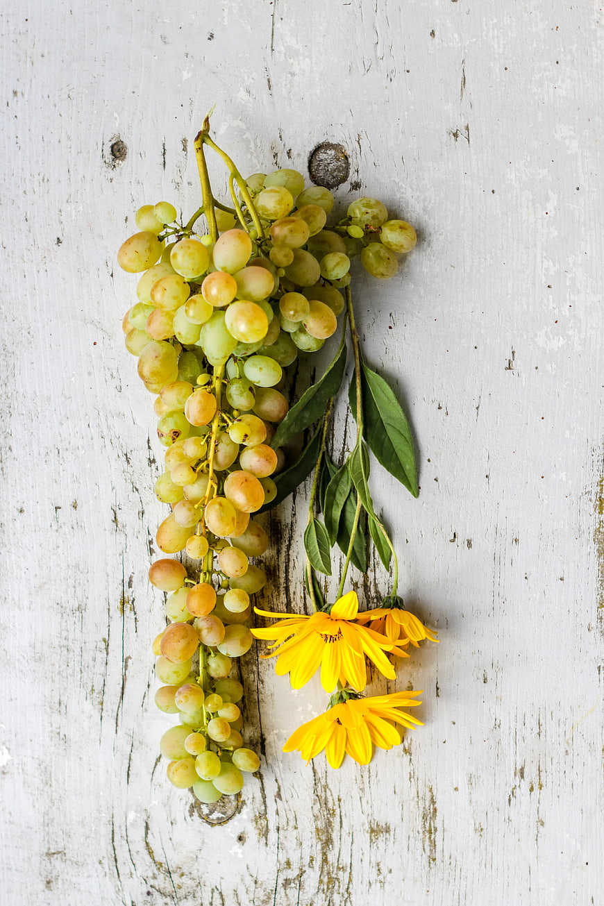 Fresh Green Grapes and Yellow Flowers on Rustic Wood