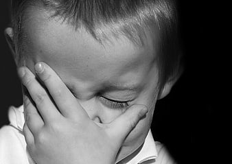 Sad child covering face with hand in black and white