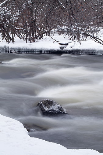 Winter river flowing with snow and icicles on banks
