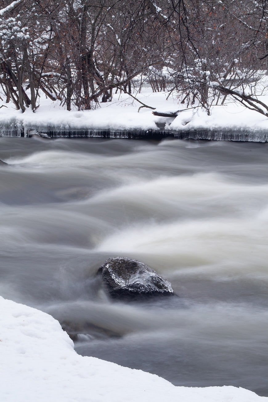 Winter river flowing with snow and icicles on banks
