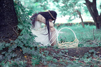 Melancholic woman in white dress sitting in forest with basket