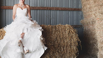 Bride in White Gown Sitting on Hay Bale in Barn
