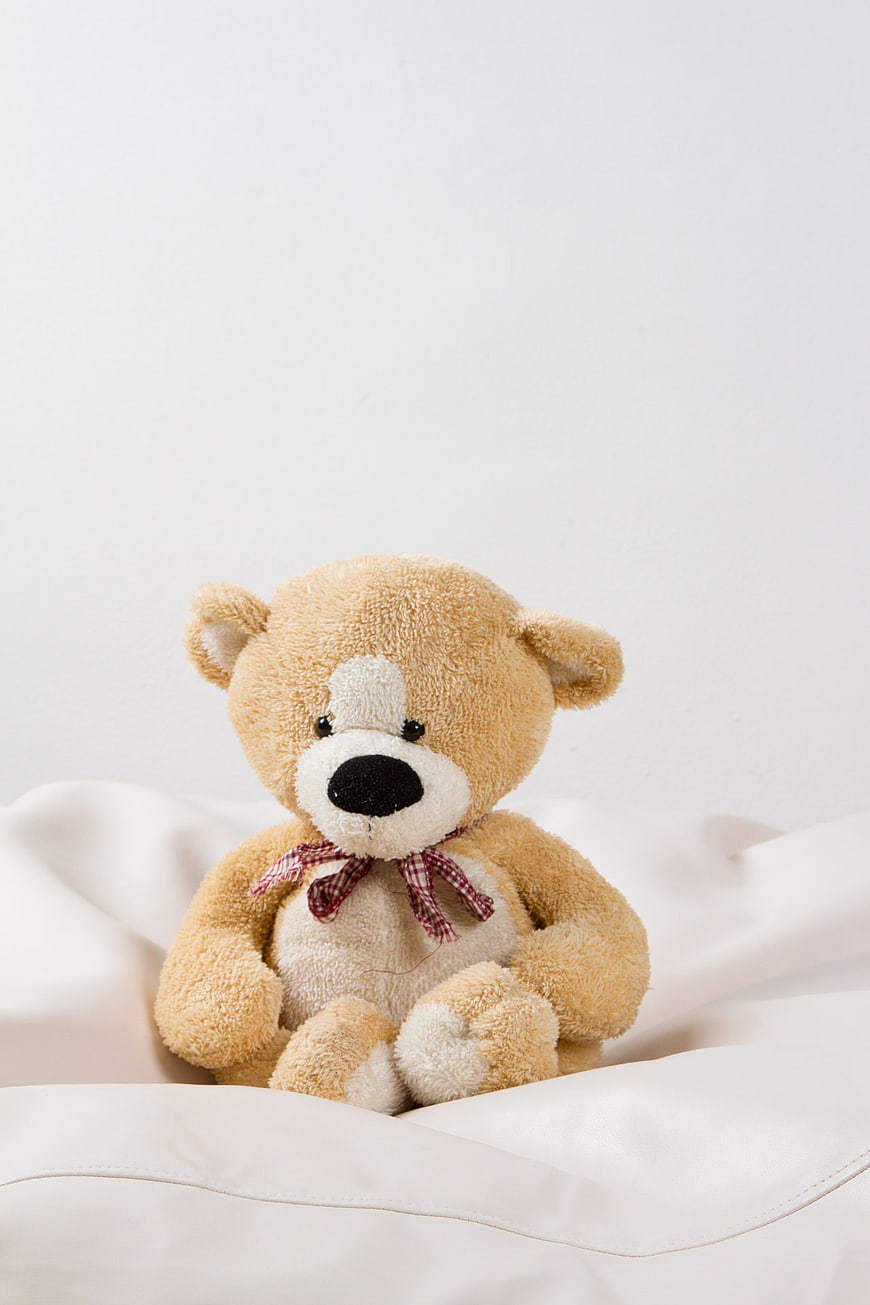 Cute Brown Teddy Bear with Plaid Bow on White Bedding