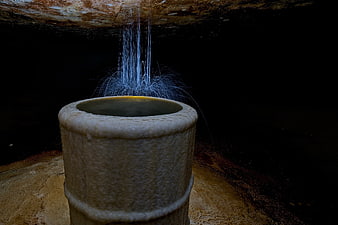 Water dripping into stone basin in dark underground cave