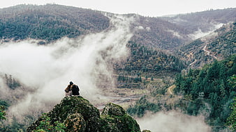 Couple sitting on rocky cliff overlooking misty mountain valley