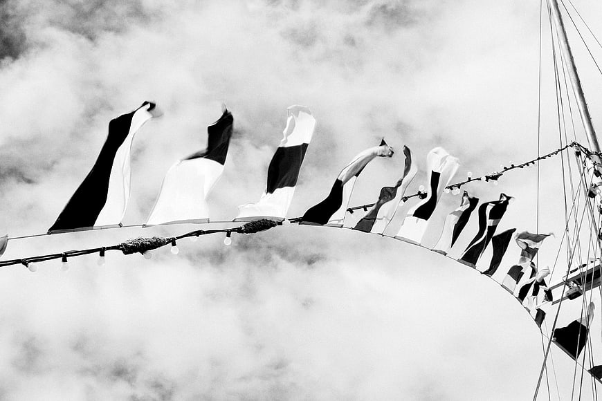 Black and white nautical flags on a sailboat against cloudy sky
