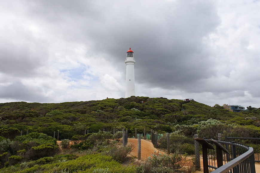 White Lighthouse on Green Hill Under Dramatic Cloudy Sky