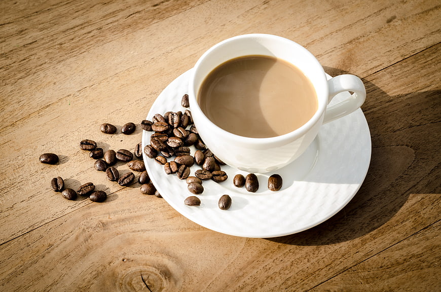 White Cup of Coffee with Beans on Wooden Table
