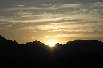 Golden sunset silhouette over mountain range with clouds