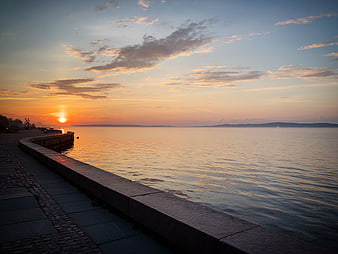 Serene Sunset Over Calm Sea With Stone Embankment