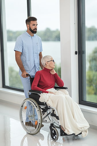 Male nurse pushing elderly woman in wheelchair by window