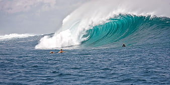 Surfers paddling in front of a massive breaking ocean wave