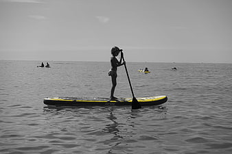 Child paddleboarding on calm sea with selective color