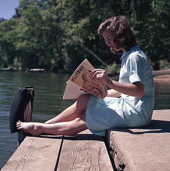 Vintage woman reading magazine on wooden dock by lake