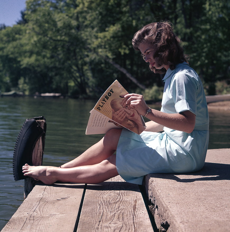 Vintage woman reading magazine on wooden dock by lake