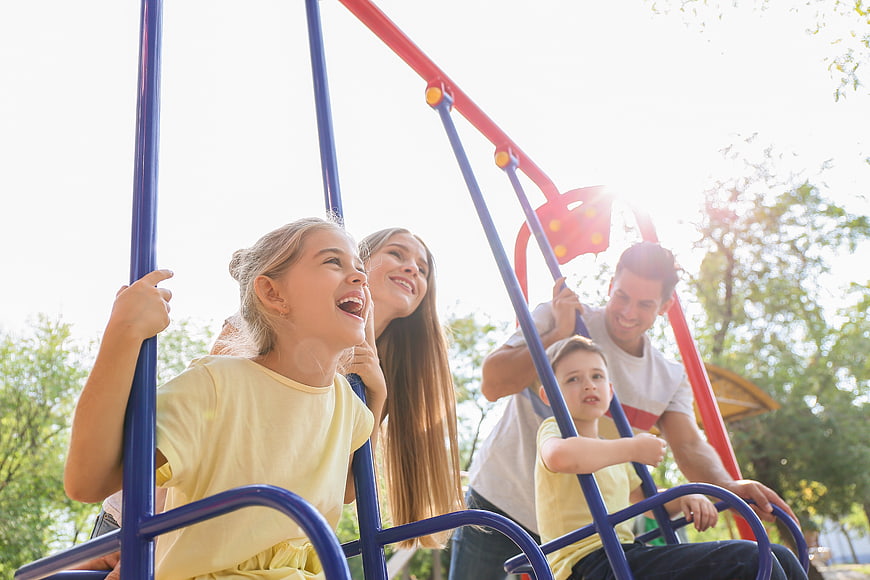 Happy family playing on swings at sunny park