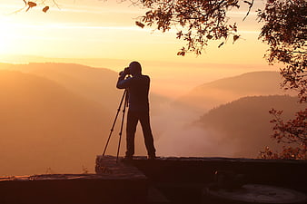 Silhouette of photographer with tripod capturing misty mountain sunrise