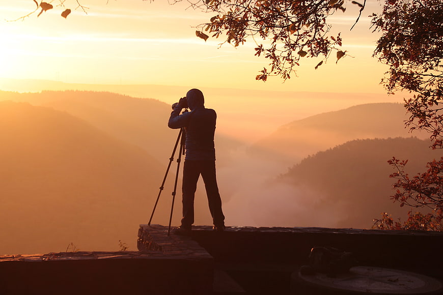 Silhouette of photographer with tripod capturing misty mountain sunrise