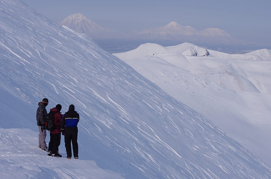 Three hikers standing on snowy mountain ridge overlooking volcanic peaks
