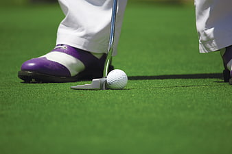Golfer putting with purple shoes on green grass