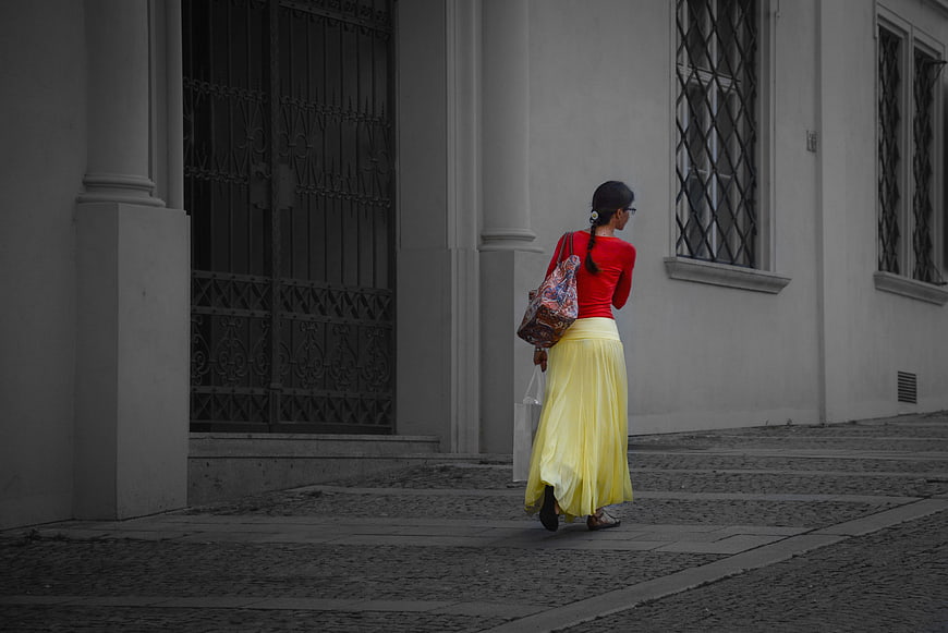 Woman in Red Top and Yellow Skirt Walking on Cobblestone Street