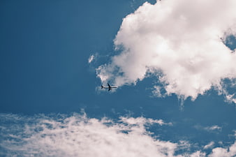 Airplane flying through blue sky with white clouds