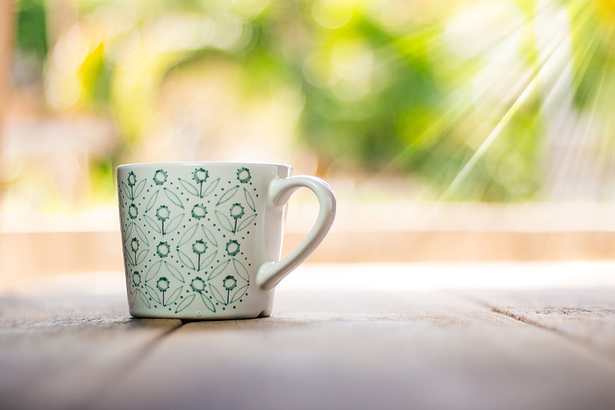 White Ceramic Coffee Cup With Green Floral Pattern On Wooden Table