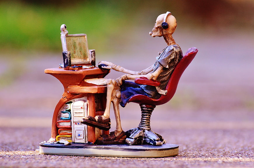 Skeleton figurine working at computer desk with headphones