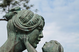 Close-up of a bronze mother and child sculpture against a cloudy sky