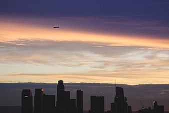 Silhouette of city skyline with airplane at sunset