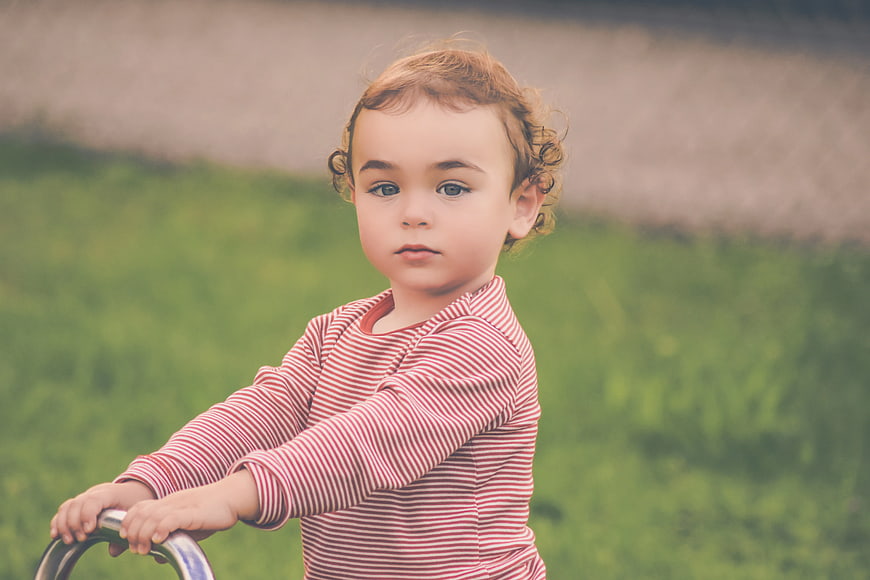 Toddler in striped shirt holding bicycle handlebars outdoors