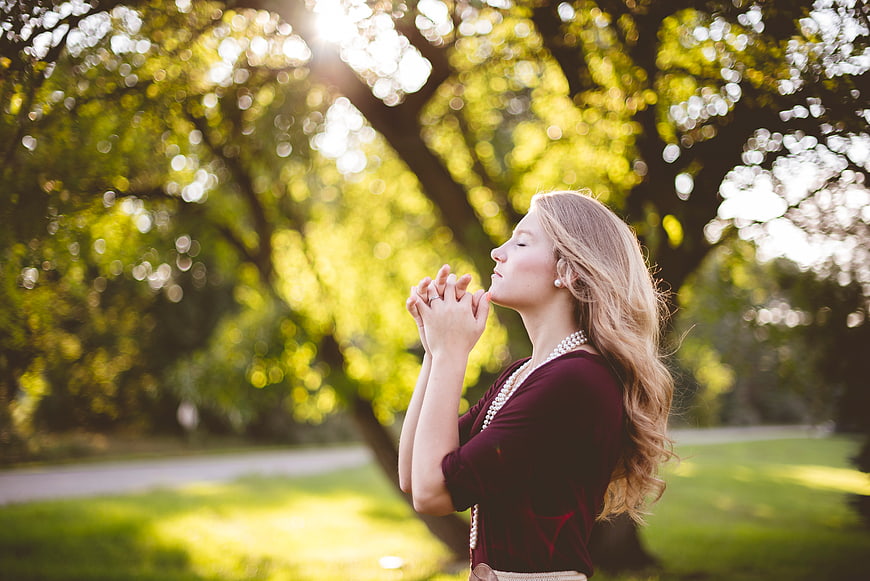 Woman Praying in Sunlit Park with Bokeh Background