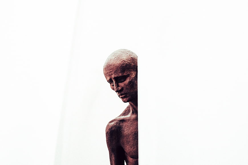 Bronze Sculpture of Emaciated Man Against White Background