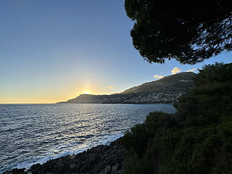 Sunset over coastal town with pine trees and rocky shore