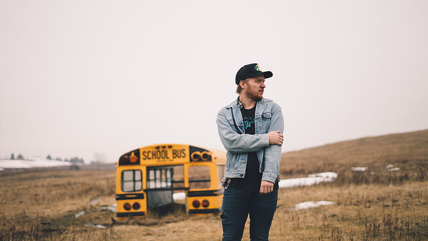 Man in Denim Jacket Standing in Field with School Bus