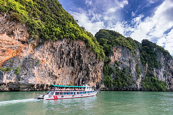 Tourist boat sailing past limestone cliffs in tropical bay