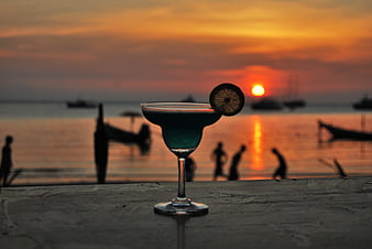 Blue cocktail with lime garnish on a wooden table at tropical beach sunset