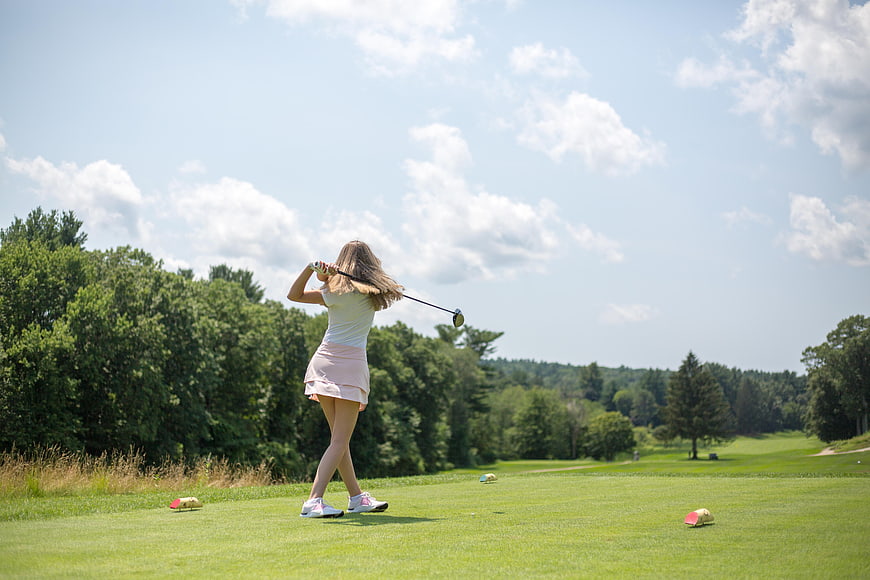 Woman Golfing on Green Course Under Blue Sky