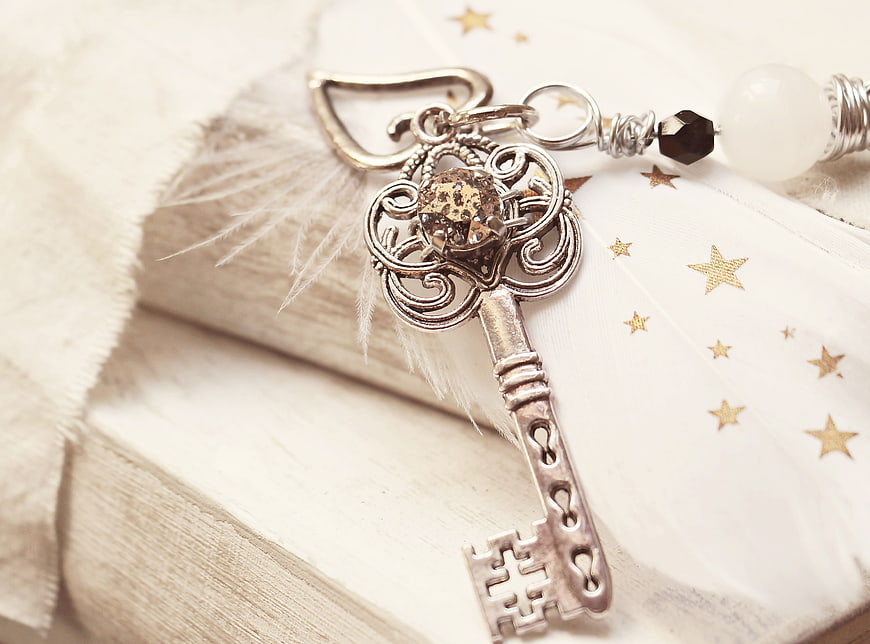 Vintage silver key charm with feather and stars on white book