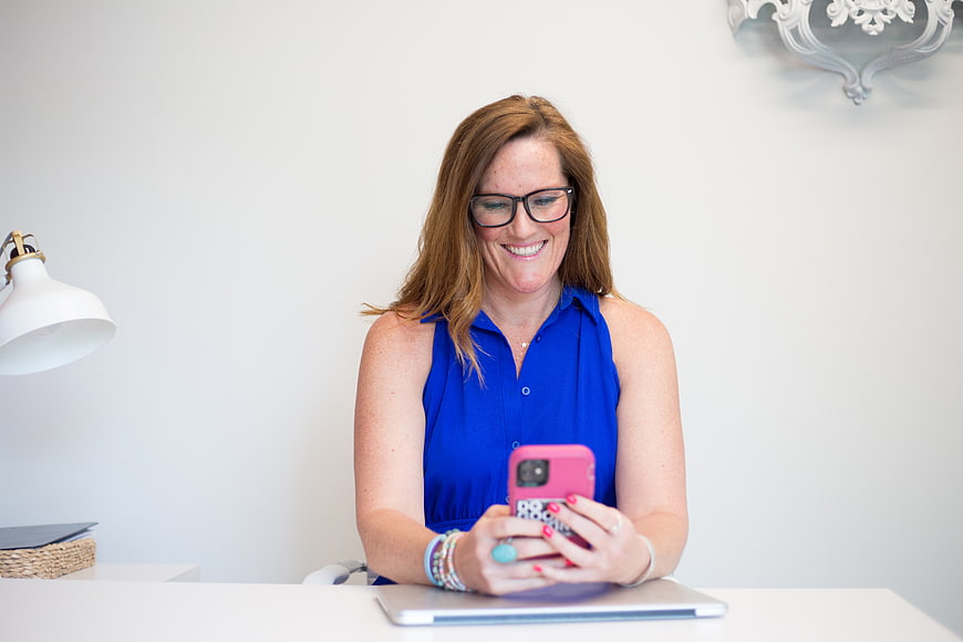 Happy woman with glasses using smartphone at desk