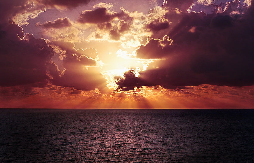 Dramatic sunset over ocean with sunbeams through clouds