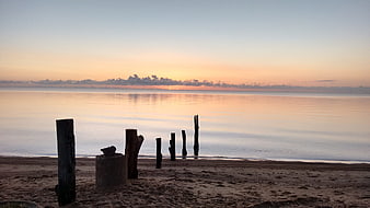 Serene Sunset Over Calm Ocean with Weathered Wooden Posts