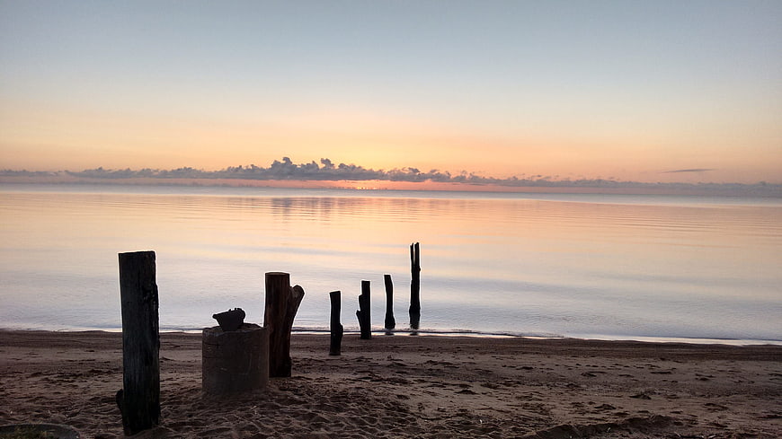 Serene Sunset Over Calm Ocean with Weathered Wooden Posts