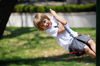 Happy young boy swinging on a chain swing in a sunny park